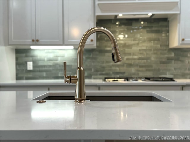 interior details featuring tasteful backsplash, sink, light stone countertops, and white cabinets