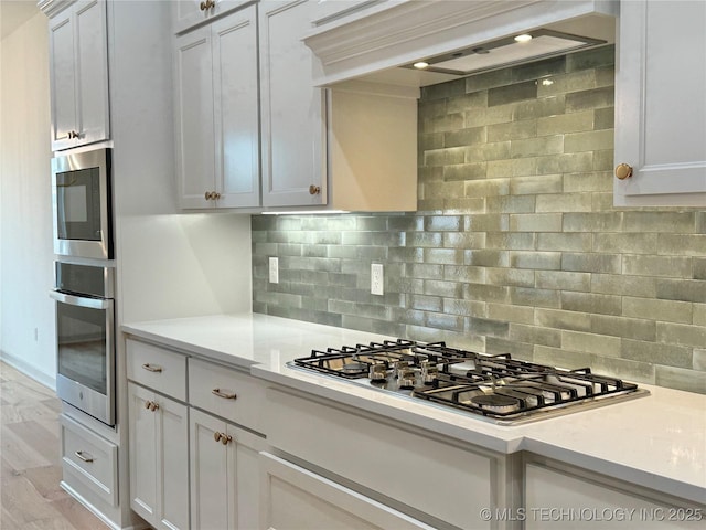 kitchen featuring light hardwood / wood-style flooring, appliances with stainless steel finishes, white cabinetry, custom range hood, and decorative backsplash