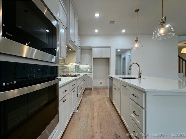 kitchen featuring sink, a kitchen island with sink, white cabinetry, stainless steel appliances, and decorative light fixtures