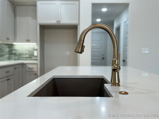 details featuring backsplash, sink, and white cabinets