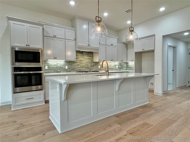 kitchen featuring sink, white cabinetry, hanging light fixtures, a center island with sink, and stainless steel appliances