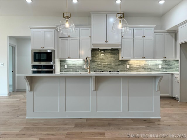 kitchen with pendant lighting, oven, an island with sink, and white cabinets