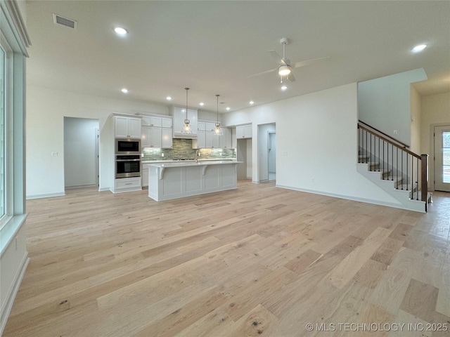 kitchen with white cabinetry, decorative light fixtures, a center island, appliances with stainless steel finishes, and backsplash