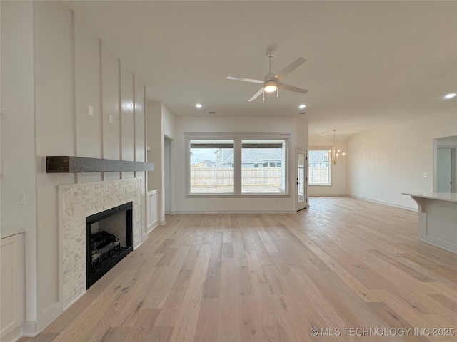 unfurnished living room with a tiled fireplace, ceiling fan with notable chandelier, and light hardwood / wood-style flooring