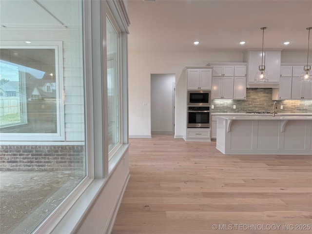 kitchen with a breakfast bar, white cabinetry, built in microwave, decorative light fixtures, and stainless steel oven