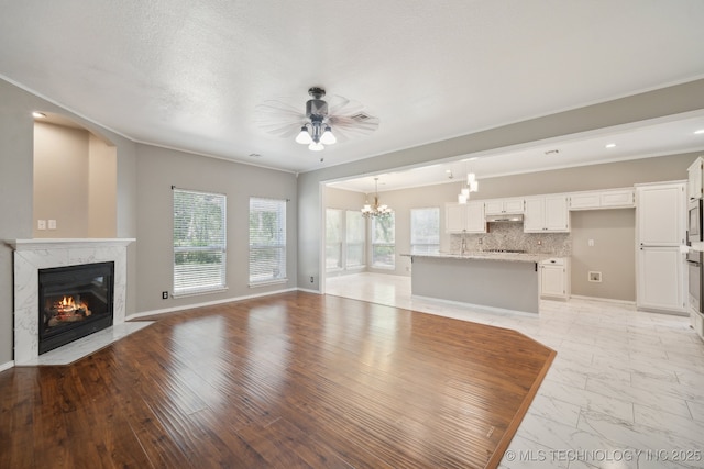 unfurnished living room with a high end fireplace, ornamental molding, ceiling fan with notable chandelier, and marble finish floor