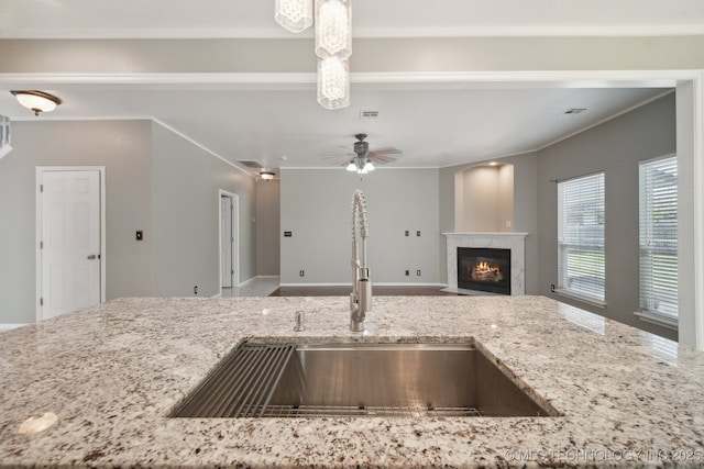 kitchen featuring crown molding, open floor plan, light stone counters, a sink, and a premium fireplace