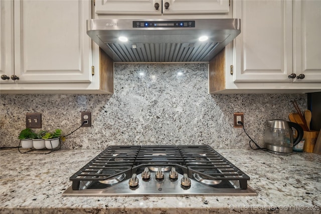 kitchen featuring white cabinetry, light stone counters, tasteful backsplash, stainless steel gas cooktop, and exhaust hood