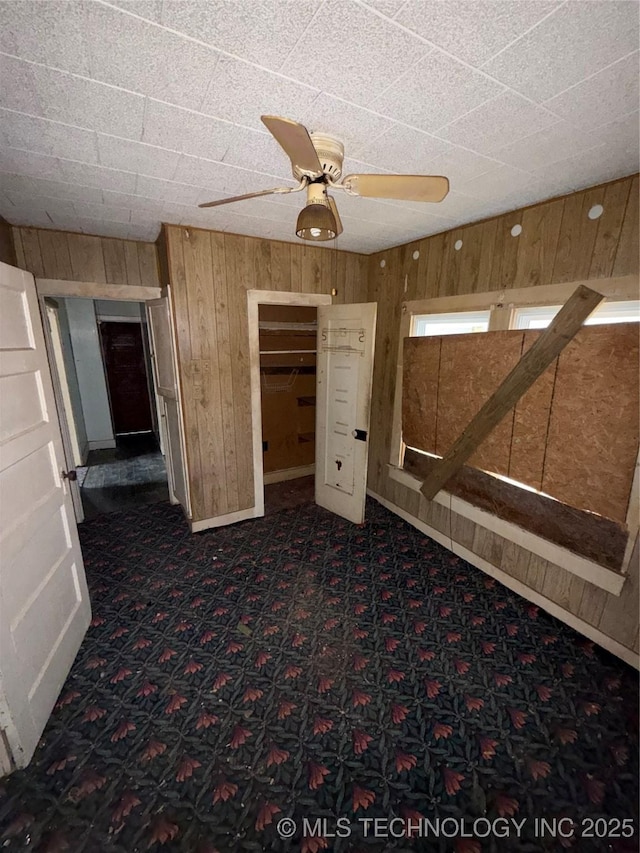 interior space featuring ceiling fan and wood walls