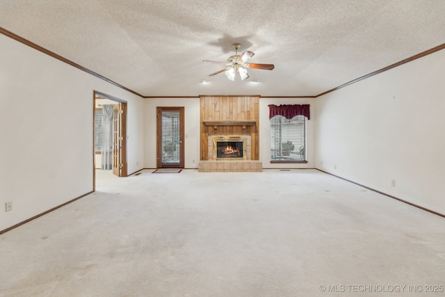 unfurnished living room with crown molding, a textured ceiling, ceiling fan, a tile fireplace, and light colored carpet