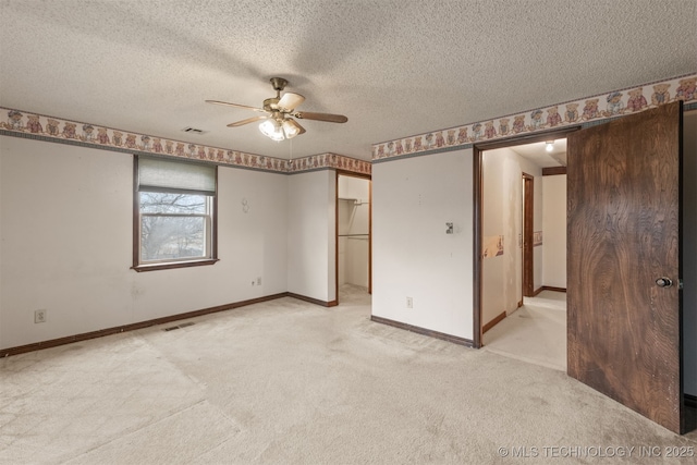 unfurnished bedroom featuring a walk in closet, light colored carpet, ceiling fan, a barn door, and a textured ceiling