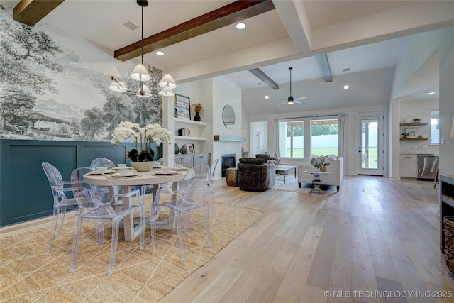 dining room with beamed ceiling, a large fireplace, ceiling fan with notable chandelier, and light hardwood / wood-style floors