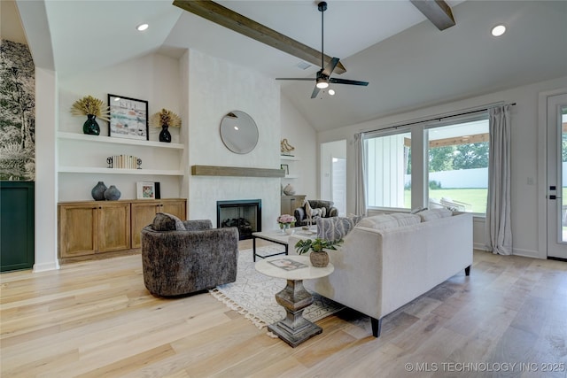 living room with beamed ceiling, a large fireplace, and light hardwood / wood-style floors