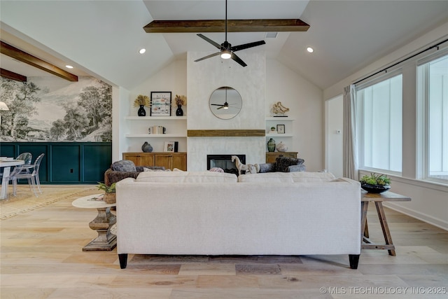 living room featuring ceiling fan, a large fireplace, light hardwood / wood-style flooring, and vaulted ceiling with beams