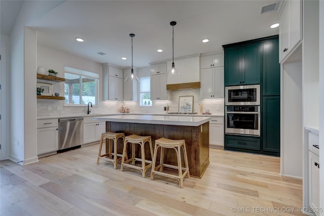 kitchen with appliances with stainless steel finishes, a center island, white cabinets, and decorative light fixtures