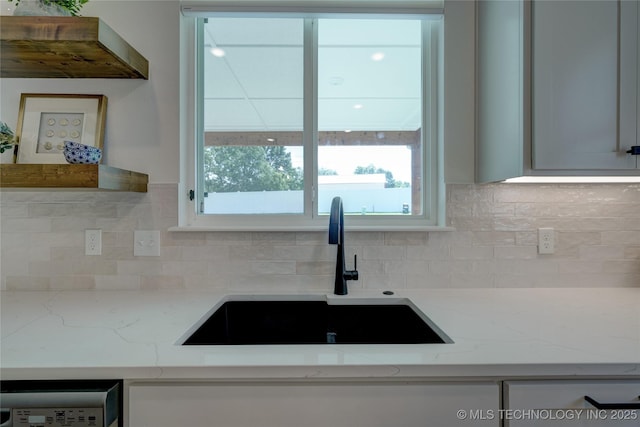 kitchen featuring a healthy amount of sunlight, light stone countertops, sink, and decorative backsplash