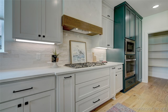 kitchen with light hardwood / wood-style flooring, custom range hood, stainless steel appliances, decorative backsplash, and white cabinets