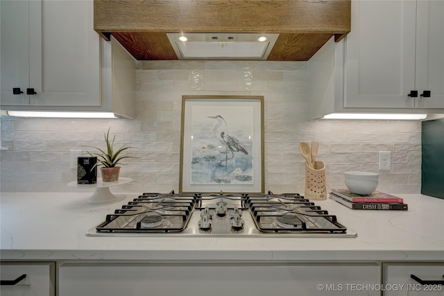 kitchen with light stone counters, stainless steel gas stovetop, custom range hood, and white cabinets