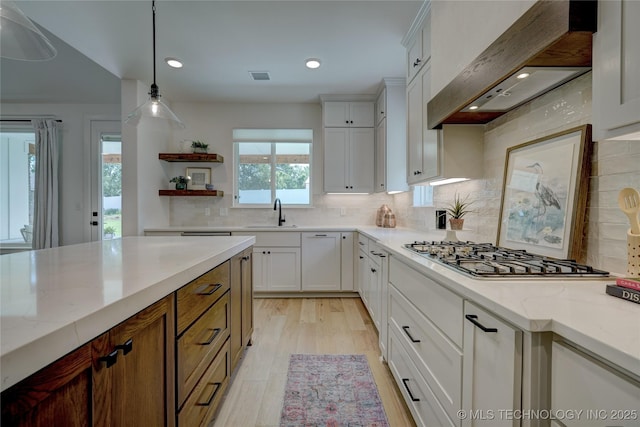 kitchen featuring pendant lighting, white cabinets, custom exhaust hood, stainless steel gas cooktop, and light stone counters