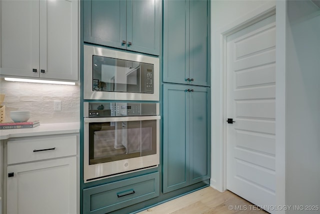 kitchen with backsplash, light wood-type flooring, white cabinets, and appliances with stainless steel finishes