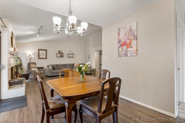 dining space featuring a brick fireplace, hardwood / wood-style floors, lofted ceiling, and a textured ceiling