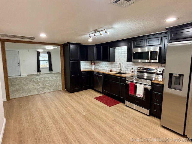 kitchen with sink, tasteful backsplash, light hardwood / wood-style flooring, a textured ceiling, and stainless steel appliances