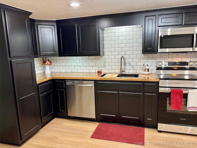 kitchen with sink, backsplash, stainless steel appliances, light hardwood / wood-style floors, and wood counters