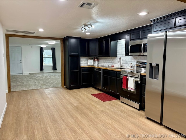 kitchen with appliances with stainless steel finishes, sink, decorative backsplash, light hardwood / wood-style floors, and a textured ceiling