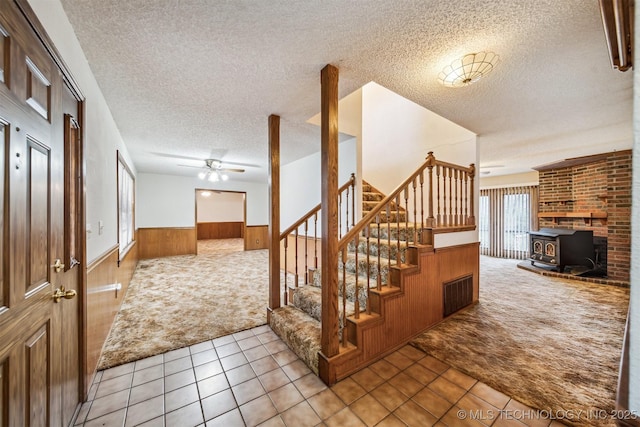 interior space featuring ceiling fan, a wood stove, a textured ceiling, and wood walls