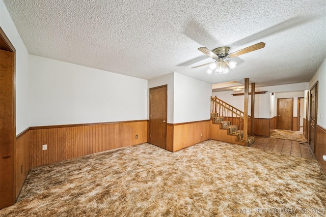 carpeted spare room featuring ceiling fan, a textured ceiling, and wooden walls