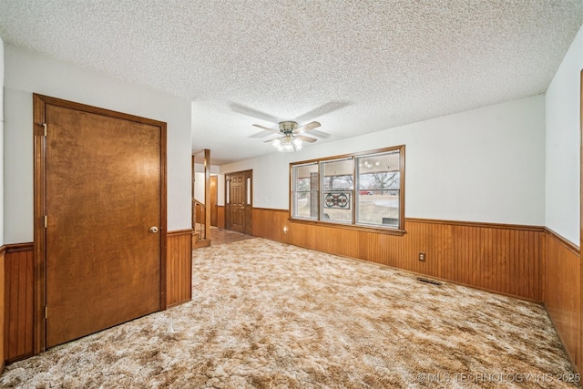 carpeted spare room with ceiling fan, a textured ceiling, and wooden walls