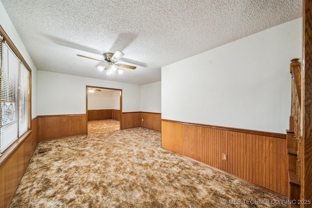 carpeted empty room featuring ceiling fan, a textured ceiling, and wooden walls