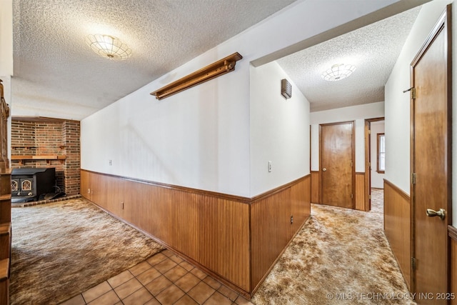 hall featuring wooden walls, light carpet, and a textured ceiling