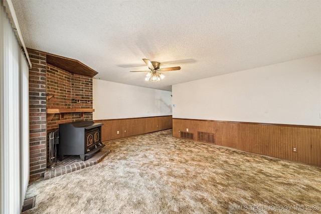 unfurnished living room featuring wooden walls, a wood stove, and dark colored carpet