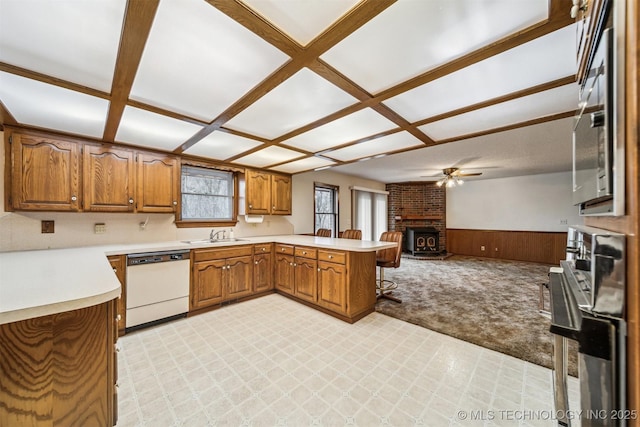 kitchen featuring wooden walls, dishwasher, coffered ceiling, kitchen peninsula, and light carpet