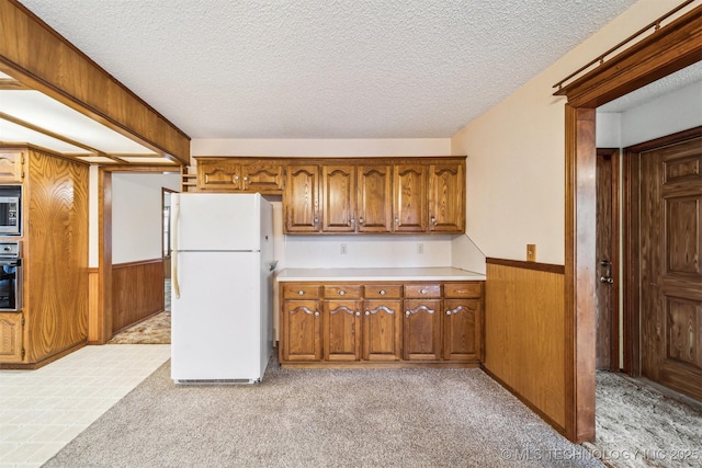 kitchen featuring white refrigerator, wall oven, wooden walls, and light carpet