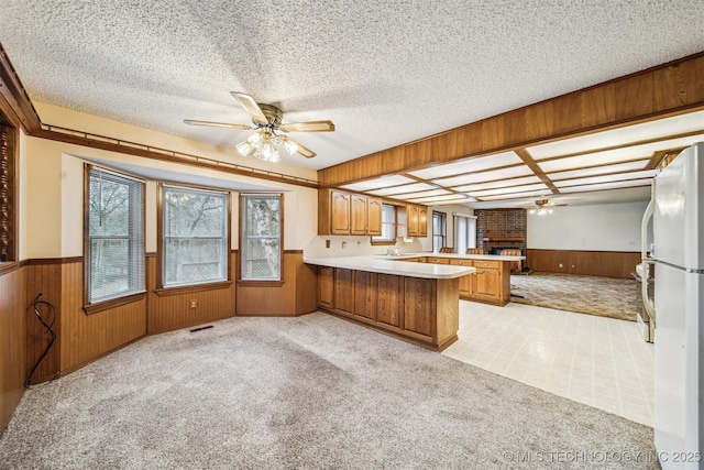 kitchen with wood walls, a textured ceiling, kitchen peninsula, white fridge, and ceiling fan