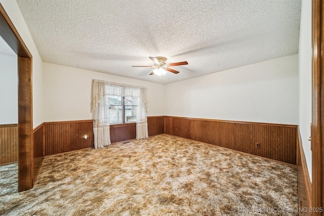 carpeted spare room featuring ceiling fan, a textured ceiling, and wood walls