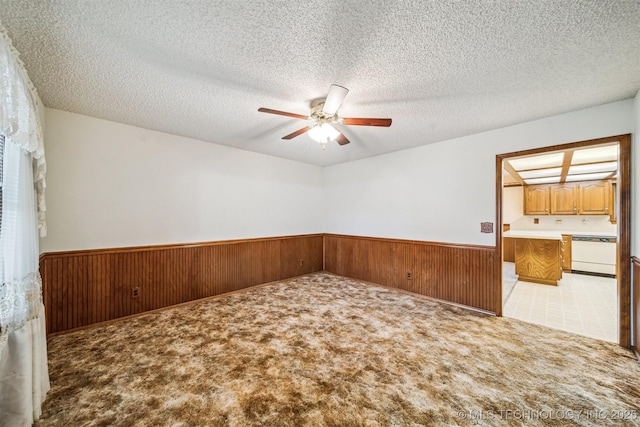 empty room featuring ceiling fan, light colored carpet, a textured ceiling, and wood walls