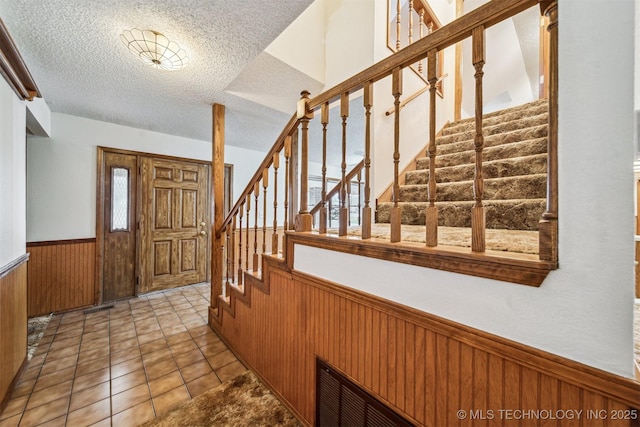 entrance foyer featuring light tile patterned floors, wooden walls, a textured ceiling, and plenty of natural light