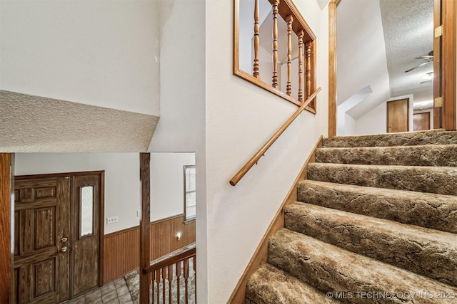 stairs featuring a textured ceiling and wood walls