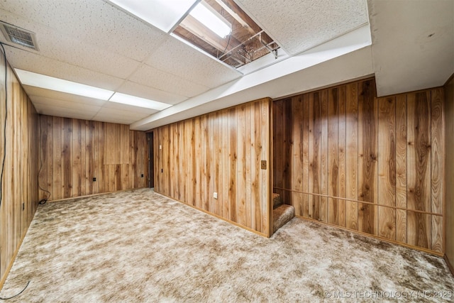 basement featuring carpet, a drop ceiling, and wooden walls