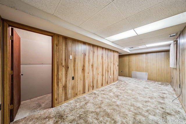 basement featuring carpet flooring, a paneled ceiling, and wood walls