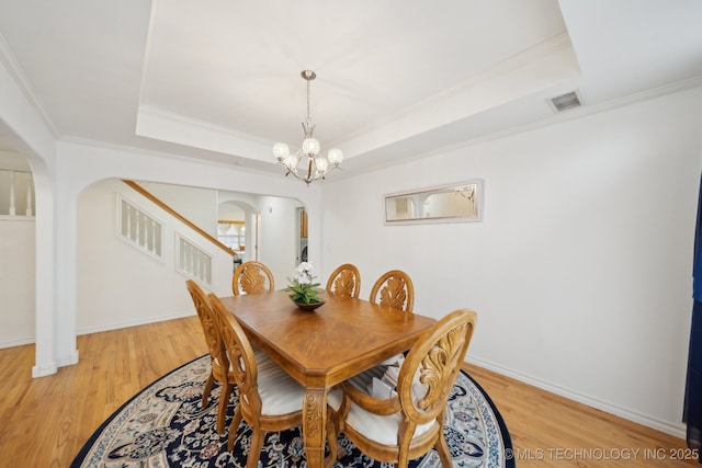 dining space with ornamental molding, light hardwood / wood-style flooring, an inviting chandelier, and a tray ceiling