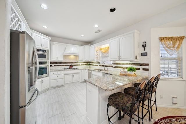 kitchen featuring sink, stainless steel appliances, light stone countertops, white cabinets, and kitchen peninsula