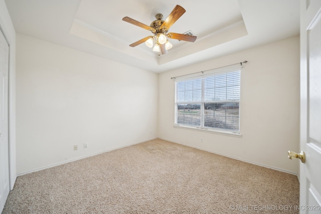 empty room with crown molding, ceiling fan, a tray ceiling, and carpet