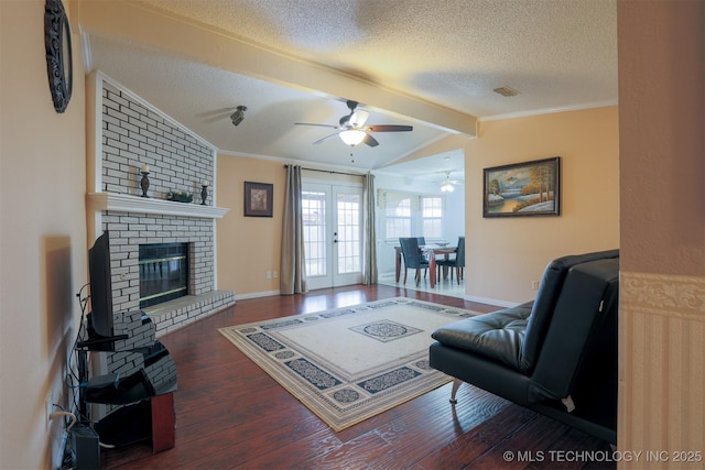 living room featuring dark wood-type flooring, french doors, vaulted ceiling with beams, a brick fireplace, and a textured ceiling