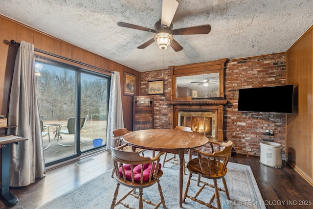 dining area with dark hardwood / wood-style floors, a textured ceiling, a fireplace, and wood walls