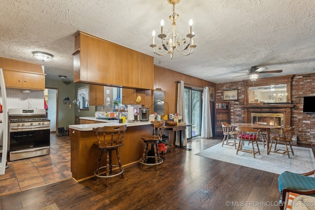 kitchen with a kitchen bar, stainless steel gas stove, dark hardwood / wood-style flooring, kitchen peninsula, and ceiling fan with notable chandelier