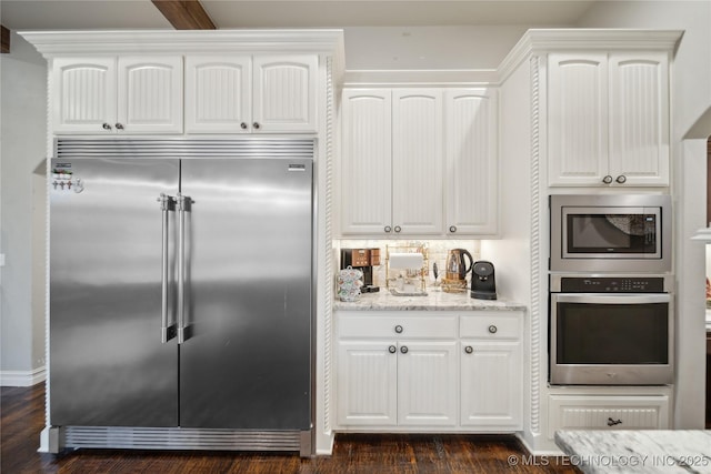 kitchen with tasteful backsplash, light stone counters, built in appliances, dark hardwood / wood-style floors, and white cabinets